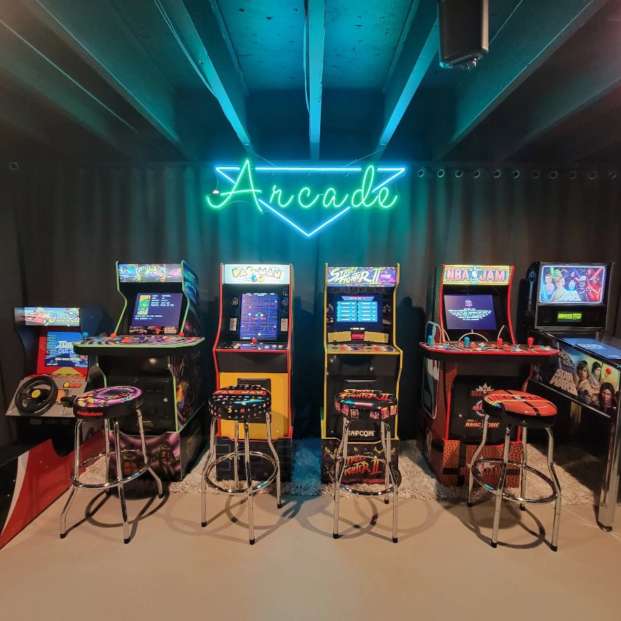 A green and blue LED neon sign that says “Arcade” mounted above a row of vintage arcade machines in a game room with a dark ceiling and retro stools. Perfect for gaming rooms, arcades, man caves, and entertainment setups.