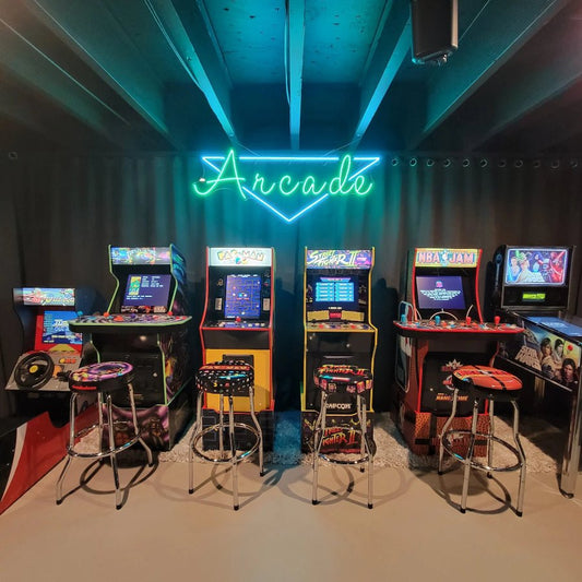 A green and blue LED neon sign that says “Arcade” mounted above a row of vintage arcade machines in a game room with a dark ceiling and retro stools. Perfect for gaming rooms, arcades, man caves, and entertainment setups.